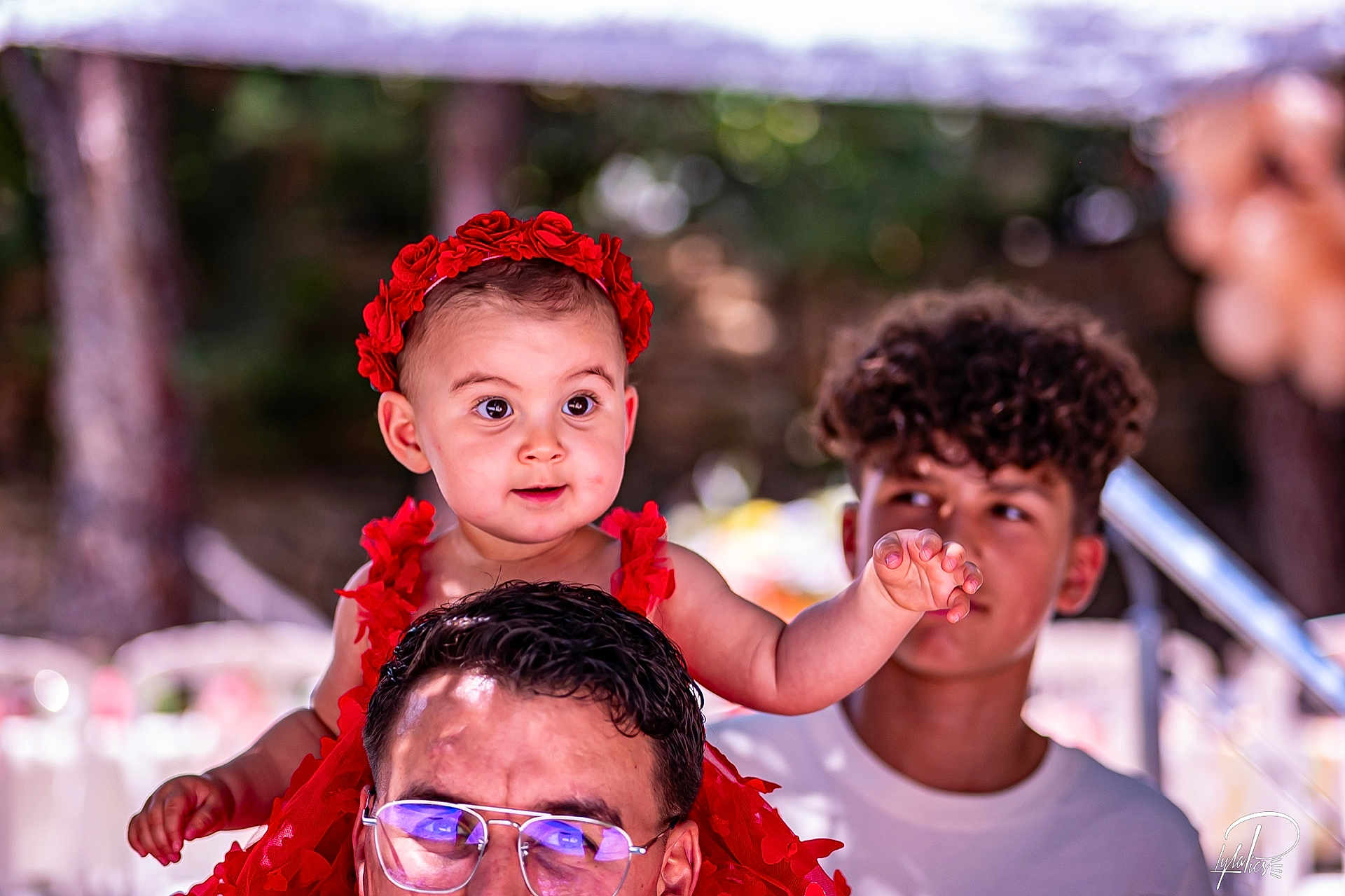 Mélia a rejoint le concours — aidez-le/la à gagner de superbes lots ! baby, child, man, teenager, red_dress, flower_headband, glasses, curly_hair, outdoor, portrait, people, smiling, shoulders, reaching_hand, background_blur, daylight, family, happy, casual_clothing, nature