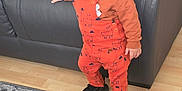 Demir joined the competition — help win amazing prizes! toddler, child, standing, orange_overalls, llama_print, black_sneakers, smile, indoor, couch, leather, carpet, wood_floor, hand, face, hair, clothing, young_child, playful, home, person