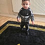 toddler, child, indoor, carpet, floor, radiator, tracksuit, adidas, black_clothing, curious_expression, standing, young_child, sporty, casual_wear, wooden_floor, patterned_rug, home_interior, portrait, person, footwear