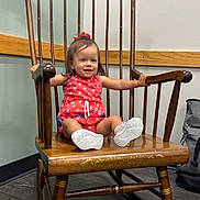 Aleigha is registered to the contest to win money with this photo: toddler, child, baby, portrait, smiling, sitting, rocking_chair, antique_furniture, wooden_chair, red_outfit, hair_bow, sneakers, indoor, hallway, wood_floor, wall, handrail, furniture, happy, photography