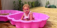 Isabelle is registered to the contest to win money with this photo: child, toddler, pool, pink_pool, water, summer, outdoor, wooden_deck, plants, fence, sunny, play, happy, splash, curly_hair, swimsuit, young_child, daytime, garden, fun