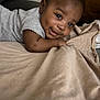baby, infant, smiling, face, blanket, cushion, indoor, child, cute, lying_down, dimples, soft_texture, cozy, person, head, curly_hair, apparel, toddler, expression, happy