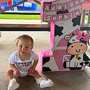 Adalynn joined the competition — help win amazing prizes! baby, child, infant, birthday, party, number_one, decoration, pink, cow, cute, outdoor, concrete_floor, table, sitting, shoes, white_clothing, celebration, banner, grass, playground