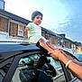 child, car, roof, hands, adult, reflection, window, street, houses, sky, evening, brick, clothing, shorts, tshirt, person, outdoor, sidewalk, residential, holding