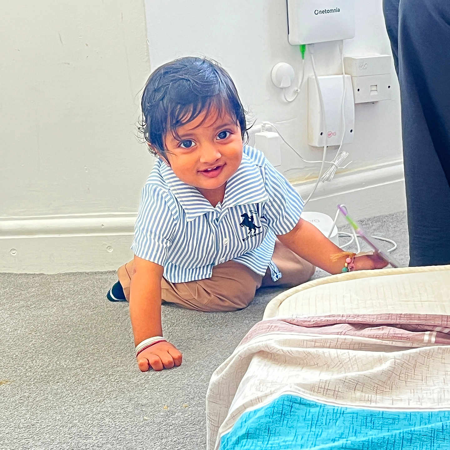 Gurshabad is registered to the contest to win money with this photo: bed, bedding, bracelet, brown_pants, carpet, child, crawling, curiosity, cute, device, floor, home, indoor, person, smile, striped_shirt, toddler, wall_socket, wet_hair, young_child