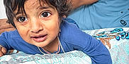 Gurshabad joined the competition — help win amazing prizes! toddler, child, bedspread, floral_pattern, blue_shirt, person, indoor, hand, bracelet, curly_hair, expression, looking, home, furniture, fabric, young_child, portrait, casual, resting, closeup