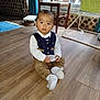 baby, child, indoor, floor, wooden_floor, vest, sitting, holding, box, window, chair, curious, person, sock, footwear, home_interior, furniture, greenery, curtain, natural_light