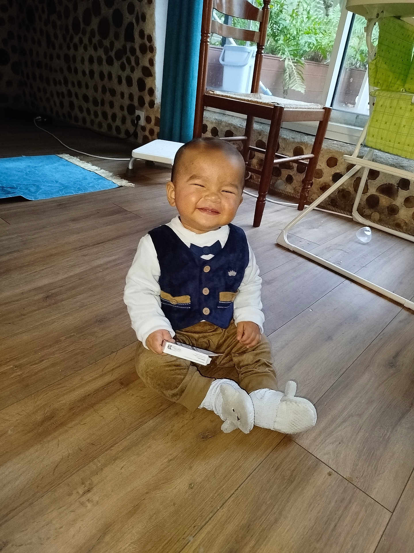 Haroun a rejoint le concours — aidez-le/la à gagner de superbes lots ! baby, child, smiling, sitting, indoor, wooden_floor, vest, pants, sock, toy, chair, high_chair, curtain, window, plant, home, floor, person, cute, happy