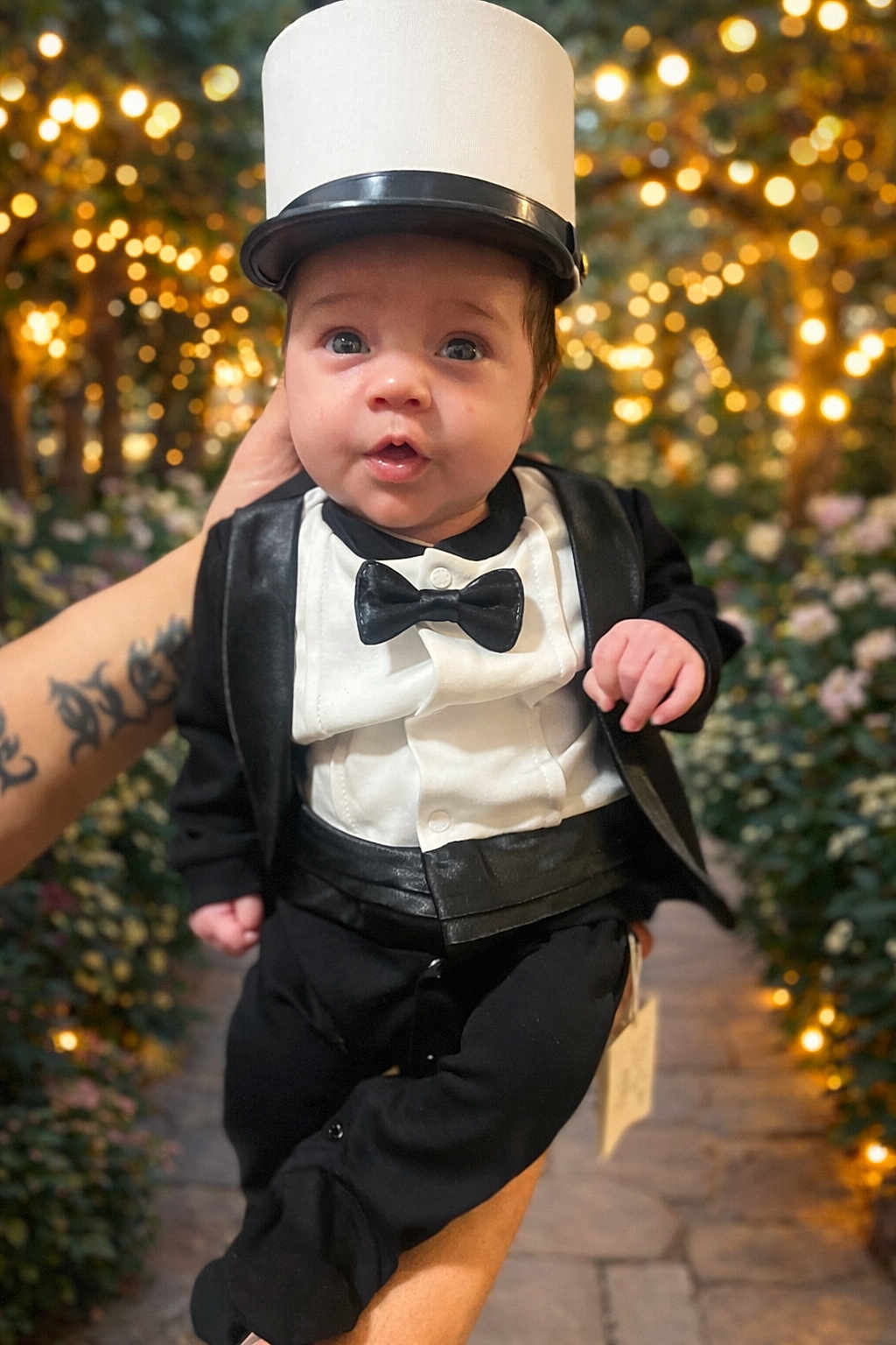 Alessyo a rejoint le concours — aidez-le/la à gagner de superbes lots ! baby, infant, child, tuxedo, bow_tie, top_hat, formal_wear, suit, bokeh, string_lights, flowers, floral_path, hand, tattoo, portrait, close_up, cute, wide_eyes, celebration, evening