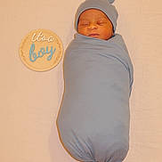 Wamala joined the competition — help win amazing prizes! newborn, baby, swaddled, sleeping, blue, hat, sign, wooden, text, neutral_background, cozy, infant, peaceful, portrait, child, cute, soft, wrapped, lying_down, announcement