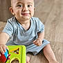 toddler, child, baby, toy, playing, smiling, indoor, floor, blue_clothing, shape_sorter, hand, foot, cute, happy, young_child, person, head, face, sitting, playtime