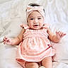 baby, child, infant, smiling, pink_dress, headband, white_bed, happy, cute, portrait, indoors, soft_texture, sitting, arms_outstretched, young_child, cheerful, clothing, headwear, person, baby_girl