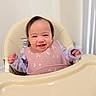baby, high_chair, smiling, bib, pink, lavender, long_sleeve, happy, child, indoor, face, person, cute, hair, seat, feeding, infant, clothing, portrait, home