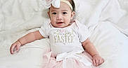 Callia is registered to the contest to win money with this photo: baby, child, infant, girl, smile, headband, flower, white_clothing, pink_skirt, tights, socks, bed, blanket, pillow, cute, portrait, indoors, soft_light, easter, happy