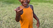 Lénaëlle participe au concours pour gagner de l'argent avec cette photo : afro_hairstyle, candid, child, curly_hair, eyes, face, grass, green_background, happy, orange_outfit, outdoors, park, playful, portrait, romper, sandals, smile, standing, teeth, toddler