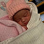 newborn, baby, sleeping, hat, blanket, pink, white, crib, knitted, infant, cozy, resting, cute, soft_lighting, indoors, child, wrapped, peaceful, portrait, closeup