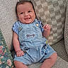 baby, child, infant, smiling, happy, portrait, sitting, chair, cushion, furniture, indoor, home, blue_clothing, overalls, shorts, patterned_fabric, floral_cushion, raised_hand, baby_face, photography
