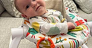 Henry is registered to the contest to win money with this photo: baby, infant, child, smiling, portrait, sitting, activity_walker, baby_toy, pacifier_toy, colorful, cushions, sofa, living_room, indoor, onesie, patterned_clothing, playtime, looking_at_camera, happy, cozy