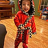 child, toddler, red_robe, checkered_trim, indoors, wooden_floor, toys, piano, window, smiling, playful, hooded_clothing, slippers, happy, person, floor, living_room, home, furniture, carpet