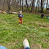 toddler, child, grass, trees, woods, beanie, overalls, toy, dog, lawn_mower, shoes, jeans, outdoor, nature, spring, forest, person, playing, daylight, casual