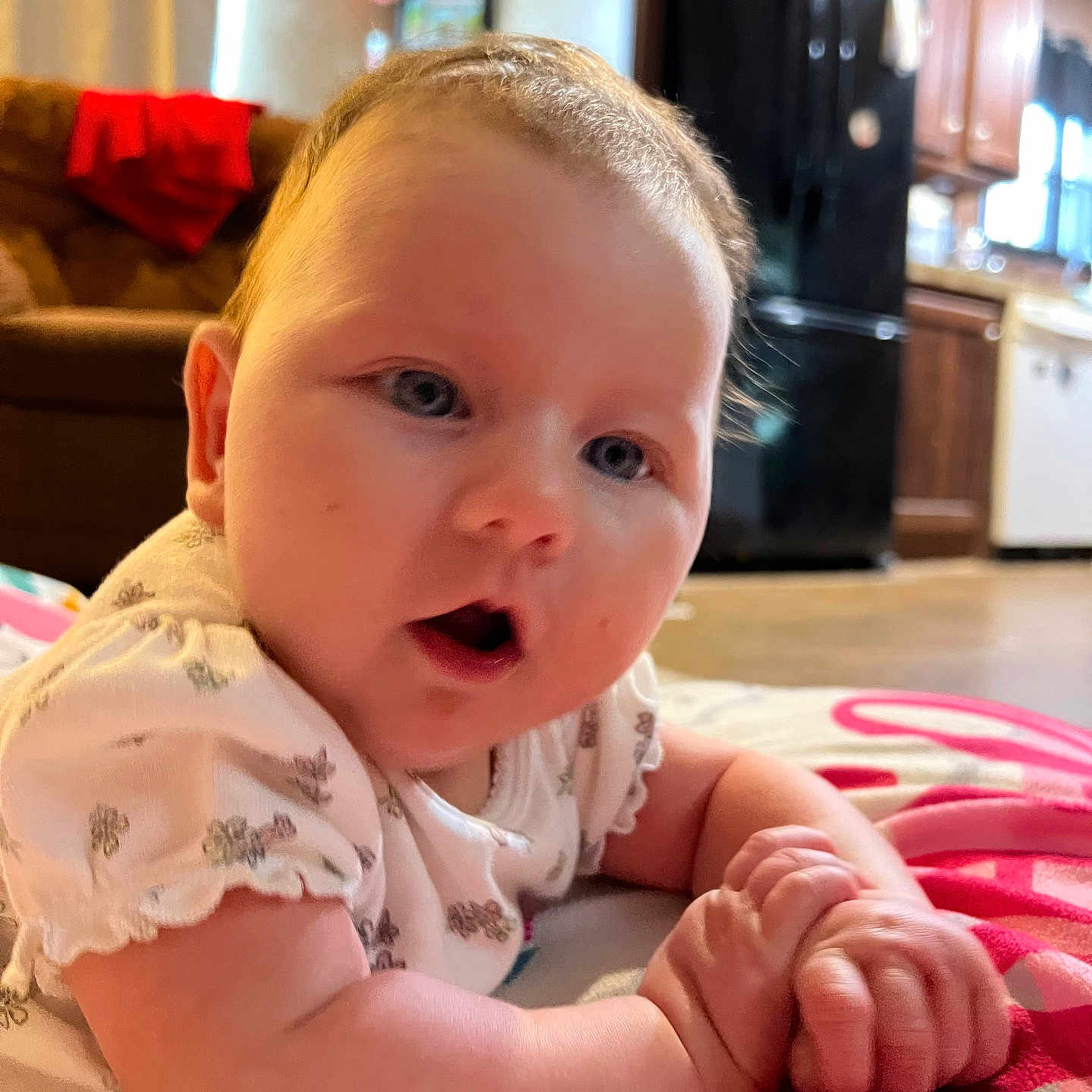 Hadley is registered to the contest to win money with this photo: appliance, baby, blanket, child, closeup, clothing, couch, curious, expression, face, furniture, hands, indoor, infant, kitchen, portrait, refrigerator, skin, soft_lighting, wooden_cabinet