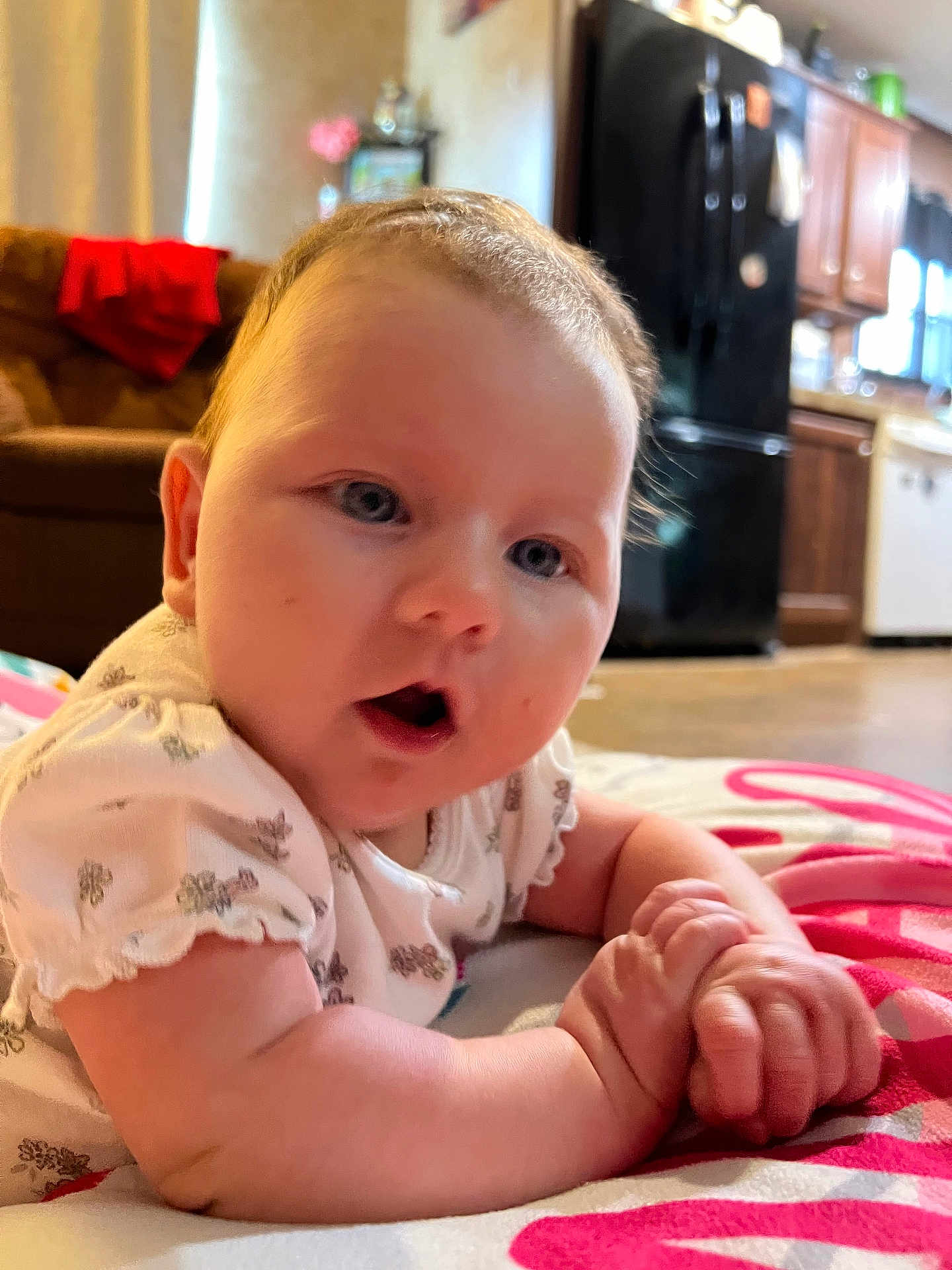 Hadley is registered to the contest to win money with this photo: baby, infant, child, face, hands, blanket, indoor, kitchen, furniture, couch, appliance, refrigerator, wooden_cabinet, expression, curious, skin, clothing, soft_lighting, closeup, portrait