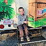 child, boy, smiling, outdoor, truck, colorful, license_plate, step, grass, casual_clothing, footwear, sunny, happy, young, vehicle, nature, seat, metal, parked, daytime