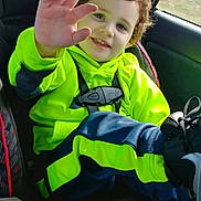 James is registered to the contest to win money with this photo: child, toddler, car_seat, bright_clothing, neon_green, navy_blue, curly_hair, smiling, waving_hand, seatbelt, car_interior, window, footwear, happy, portrait, casual_wear, young_child, safety, daylight, travel