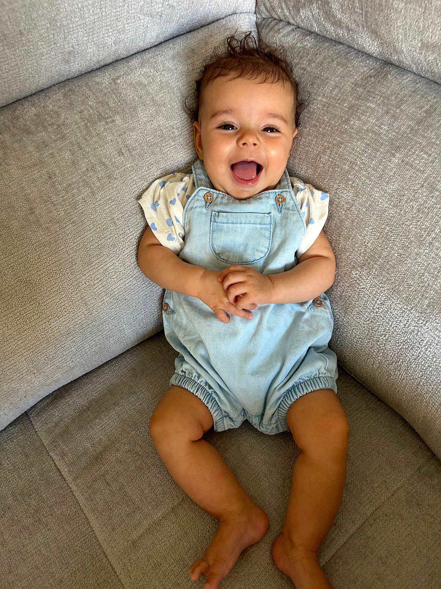Maely participe au concours pour gagner de l'argent avec cette photo : baby, child, smile, happy, romper, clothing, curly_hair, couch, furniture, indoor, person, infant, cute, skin, legs, hands, face, sitting, joyful, relaxed