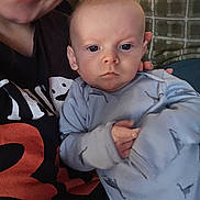 Paxton is registered to the contest to win money with this photo: baby, infant, adult, parent, onesie, hand, eyes, face, portrait, close_up, indoor, sofa, cushion, blanket, smile, casual_clothing, nose_ring, photography, holding, family