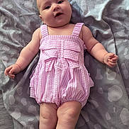 Darcie is registered to the contest to win money with this photo: arms_out, baby, blanket, child, chubby, cute, face, gray_blanket, head, indoors, infant, legs_crossed, lying_down, patterned_blanket, pink_romper, portrait, skin, smiling, soft_lighting, striped_clothing