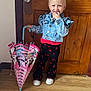 toddler, child, blonde_hair, pigtails, denim_jacket, umbrella, minnie_mouse, cherry_pattern, black_pants, white_shoes, wooden_door, wood_floor, indoor, smiling, cute, playful, standing, fashion, person, happy