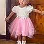 blonde_hair, bows, child, cute, fashion, floor, girl, happy, indoors, pigtails, pink_skirt, pose, smile, socks, standing, toddler, tulle_skirt, white_shoes, white_top, wooden_door