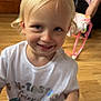 adult, baby_doll, blonde_hair, blue_eyes, cartoon_characters, casual, child, furniture, hand, happy, home, indoor, person, playful, portrait, sitting, smile, toddler, white_tshirt, wooden_floor
