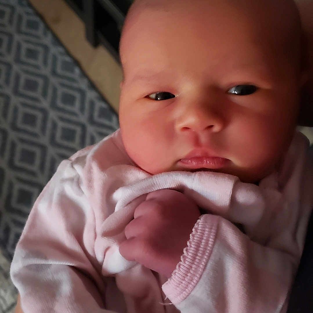 Octavia is registered to the contest to win money with this photo: baby, blanket, bodypart, bonnet, clothing, couch, face, finger, furniture, hand, hat, head, knitwear, mouth, newborn, person, photography, portrait, shelf, sweater