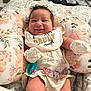 baby, smiling, bib, floral_pillow, pacifier, bedroom, blanket, mittens, clothing, infant, cute, happy, person, lying_down, soft_toys, decor, fabric, comfort, child, portrait