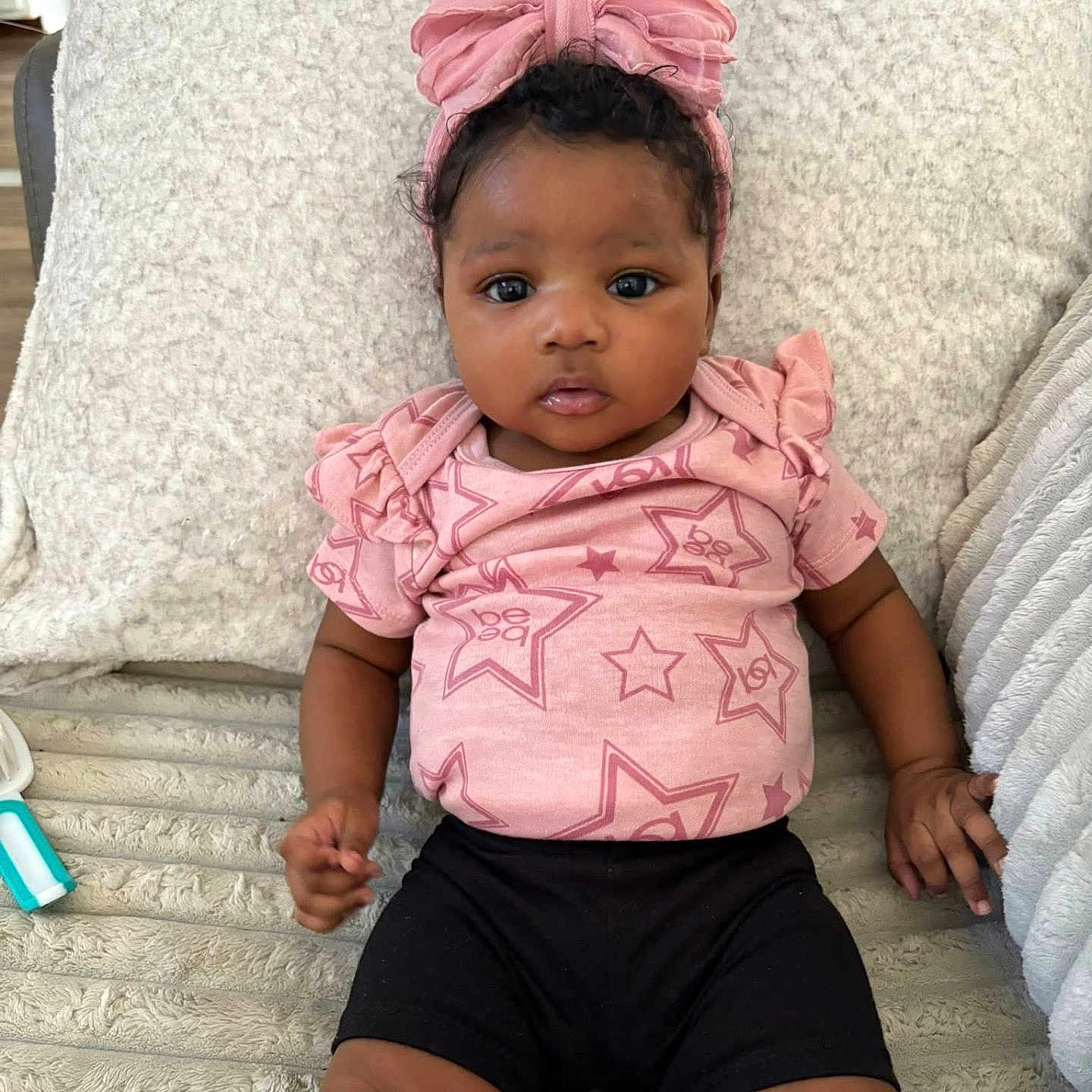 Amouraa is registered to the contest to win money with this photo: baby, black_shorts, blanket, child, comfortable, curious, cute, face, hands, headband, indoor, infant, legs, lying_down, pink_bow, pink_shirt, portrait, soft_texture, stars_pattern, young_child