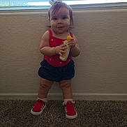 Khali is registered to the contest to win money with this photo: toddler, child, standing, carpet, red_shoes, red_top, navy_shorts, white_bow, window, blinds, bottle, indoor, wall, holding_object, infant, cute, smiling, person, young_child, hair_bow