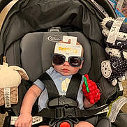 Luka is registered to the contest to win money with this photo: baby, car_seat, sunglasses, toy, infant, child, grape_toy, seatbelt, clothing, blue_onesie, black_straps, indoor, store, shopping, cute, expressionless, plush_toy, graco, sitting, childcare