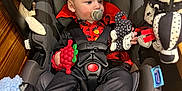 Luka is registered to the contest to win money with this photo: baby, black, blanket, car_seat, child, clothing, cute, face, footwear, head, holding, indoor, infant, pacifier, patterned, plush, red, seatbelt, sitting, toy