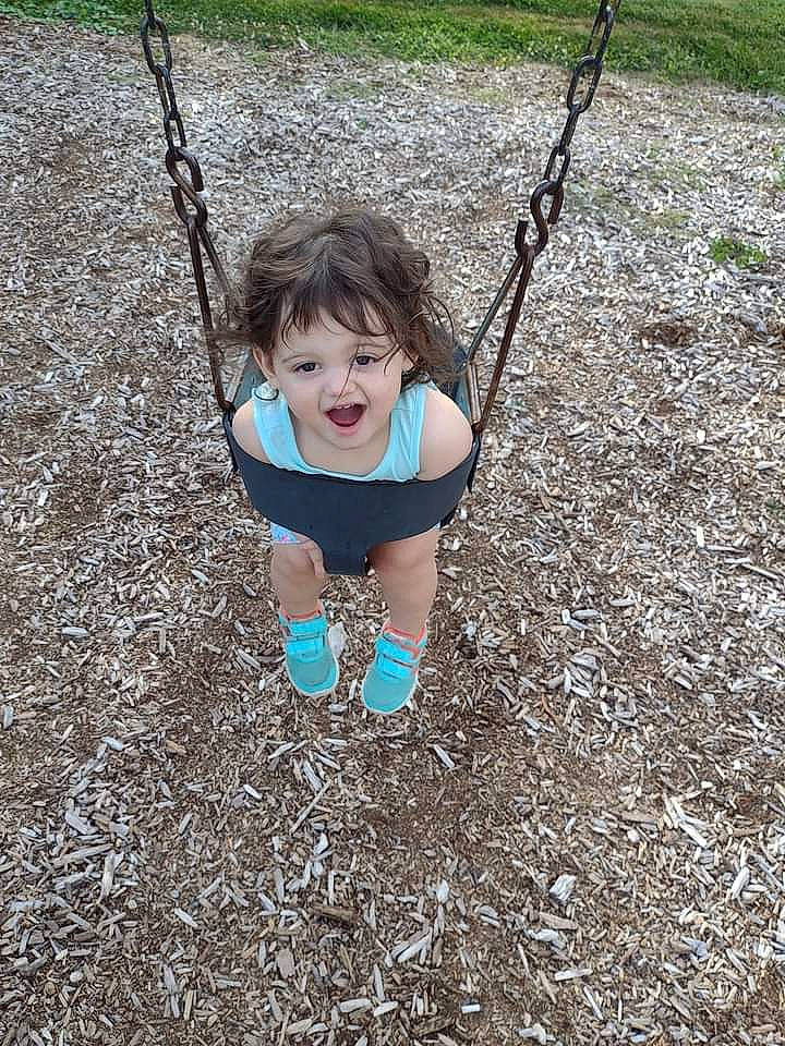 Marianna is registered to the contest to win money with this photo: baby, baby_toddler_clothing, city, electric_blue, fun, grass, happy, head, human_body, leisure, outdoor_play_equipment, people_in_nature, person, plant, play, playground, recreation, soil, swing, toddler