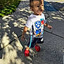 toddler, child, sidewalk, outdoor, sunlight, shadow, paw_patrol, tshirt, shorts, red_sandals, grass, concrete, summer, daylight, person, casual_clothing, standing, cute, young_child, necklace