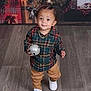 toddler, child, plaid_shirt, tan_pants, white_shoes, holiday_decor, wrapped_gifts, jingle_bell, flooring, indoor, festive, cute, standing, person, young_child, smiling, christmas, decorations, toy, portrait