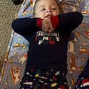 Raelyn is registered to the contest to win money with this photo: blanket, carpet, child, christmas_trees, clothing, cozy, cute, dog_pattern, face, funny_text, hands, holiday, indoors, lying_down, pajamas, person, playful, rainbow, santa_hat, smiling