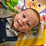 baby, infant, smiling, play_mat, colorful, cartoon, animal_print, clothing, buttoned_shirt, blue_overalls, face, head, hand, eyes, happy, cute, indoor, texture, carpet, fisherprice