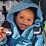 baby, child, blue_hoodie, smiling, face, stroller, happy, outdoor, clothing, person, portrait, cute, infant, seatbelt, babywear, hood, black_hair, expressive_eyes, sunlight, texture