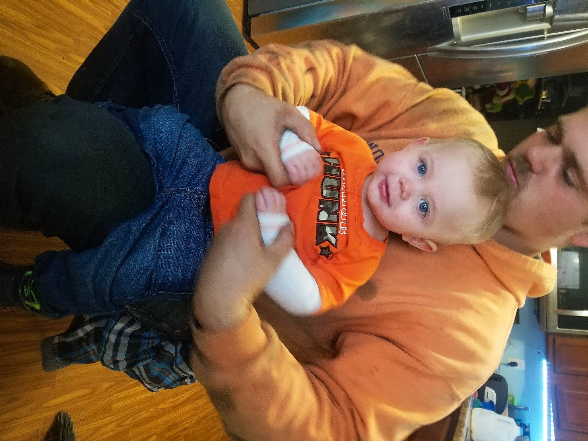 Bentley is registered to the contest to win money with this photo: baby, child, clothing, comfort, countertop, elbow, finger, flooring, fun, hardwood, hat, headwear, joint, kitchen_appliance, lap, mouth, orange, person, sitting, smile