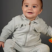 Taron joined the competition — help win amazing prizes! baby, toddler, child, portrait, studio_shot, smiling, big_eyes, zipper_jacket, onesie, sitting, bare_feet, toy, gray_background, cute, rosy_cheeks, short_hair, expression, indoor, clothing, adorable