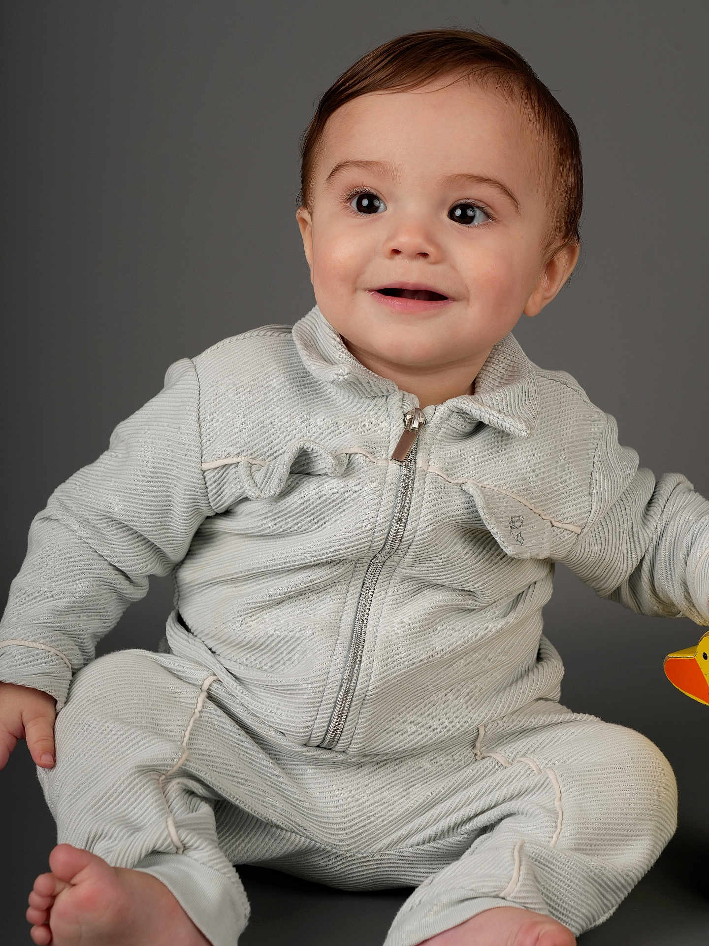 Taron joined the competition — help win amazing prizes! baby, toddler, child, portrait, studio_shot, smiling, big_eyes, zipper_jacket, onesie, sitting, bare_feet, toy, gray_background, cute, rosy_cheeks, short_hair, expression, indoor, clothing, adorable