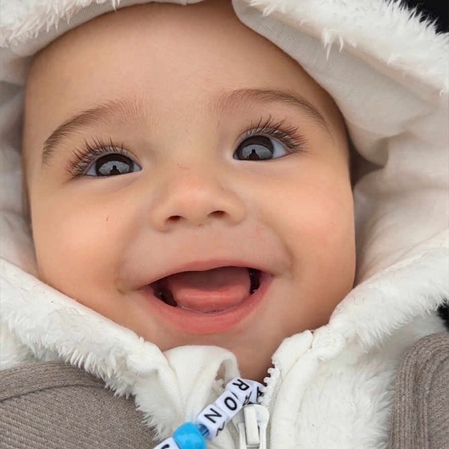 Taron-Jaques is registered to the contest to win money with this photo: baby, beads, blue, child, closeup, cute, expression, eyes, face, happy, hood, infant, jacket, joy, person, portrait, smiling, warm_clothing, white, zipper